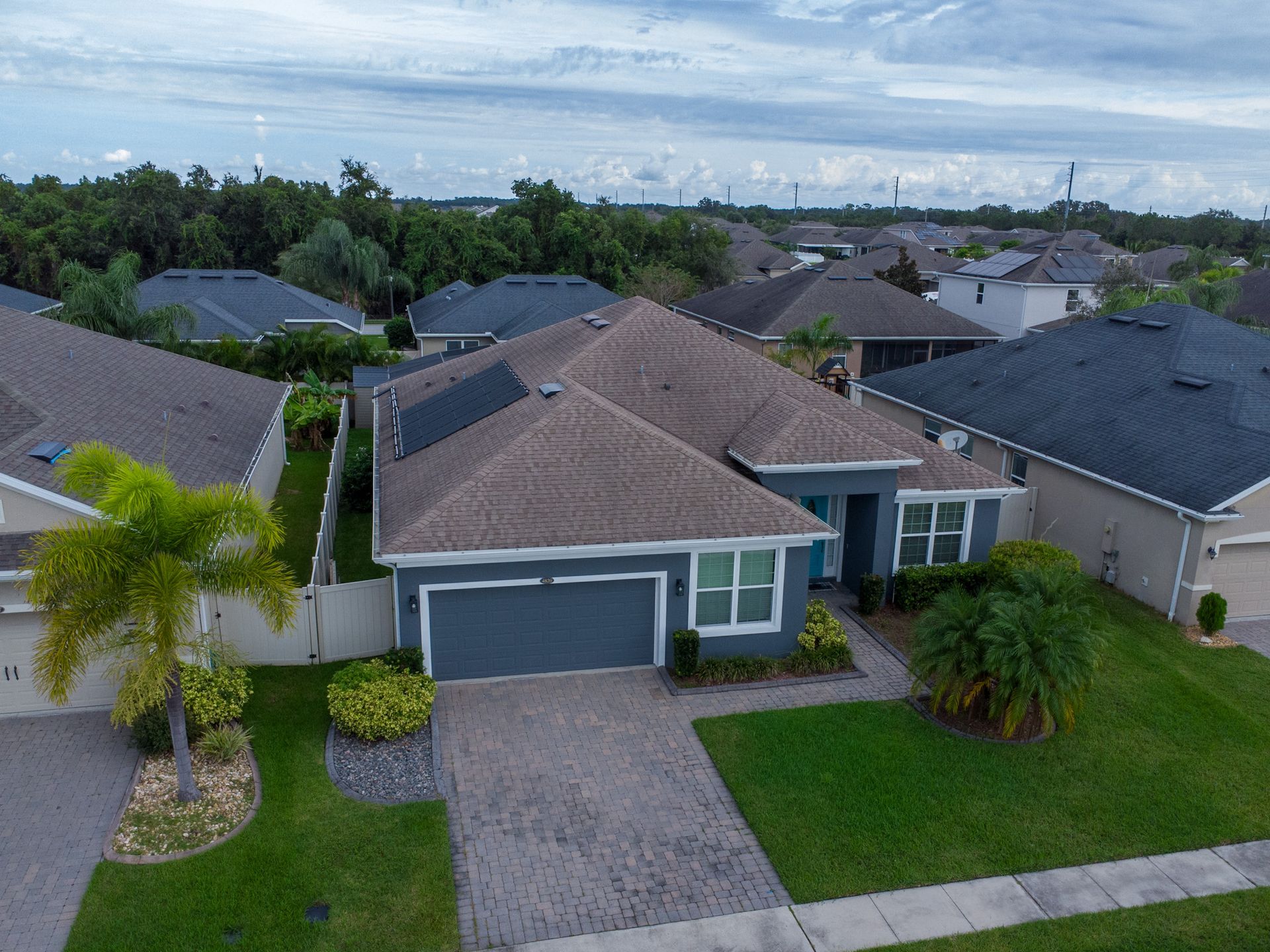 Aerial view of a blue-gray suburban house with a brown roof and green lawn.