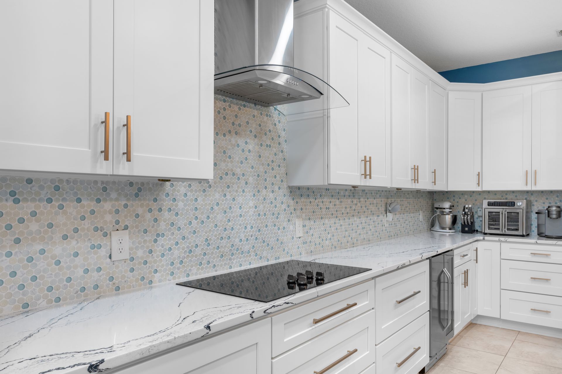 White kitchen with light countertops, backsplash, and cabinets, a range hood, and an induction cooktop.