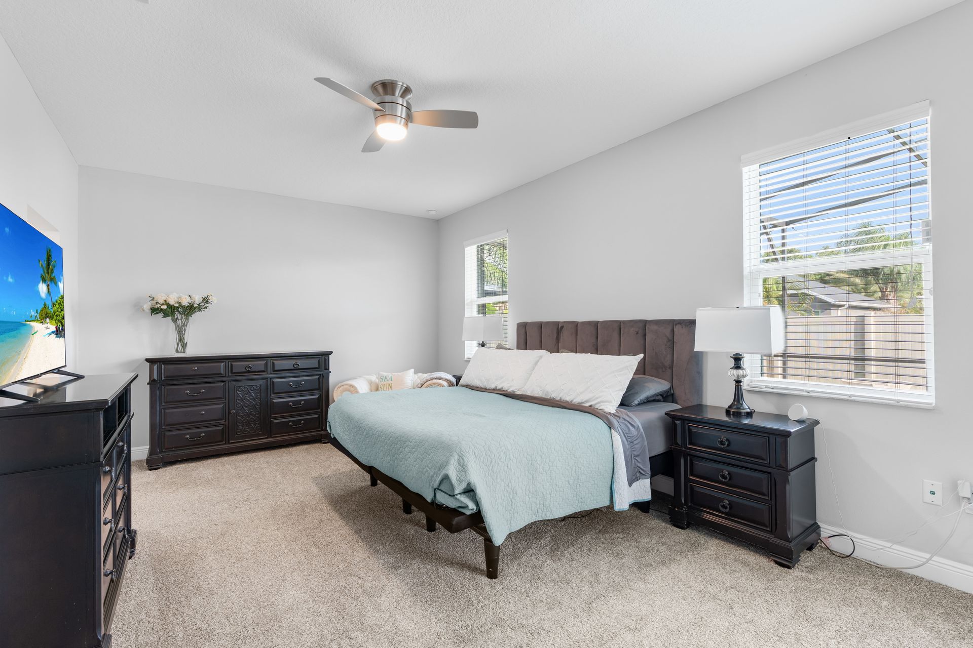 Bedroom with bed, dresser, TV, and window with blinds. Neutral colors with a light blue bedspread.