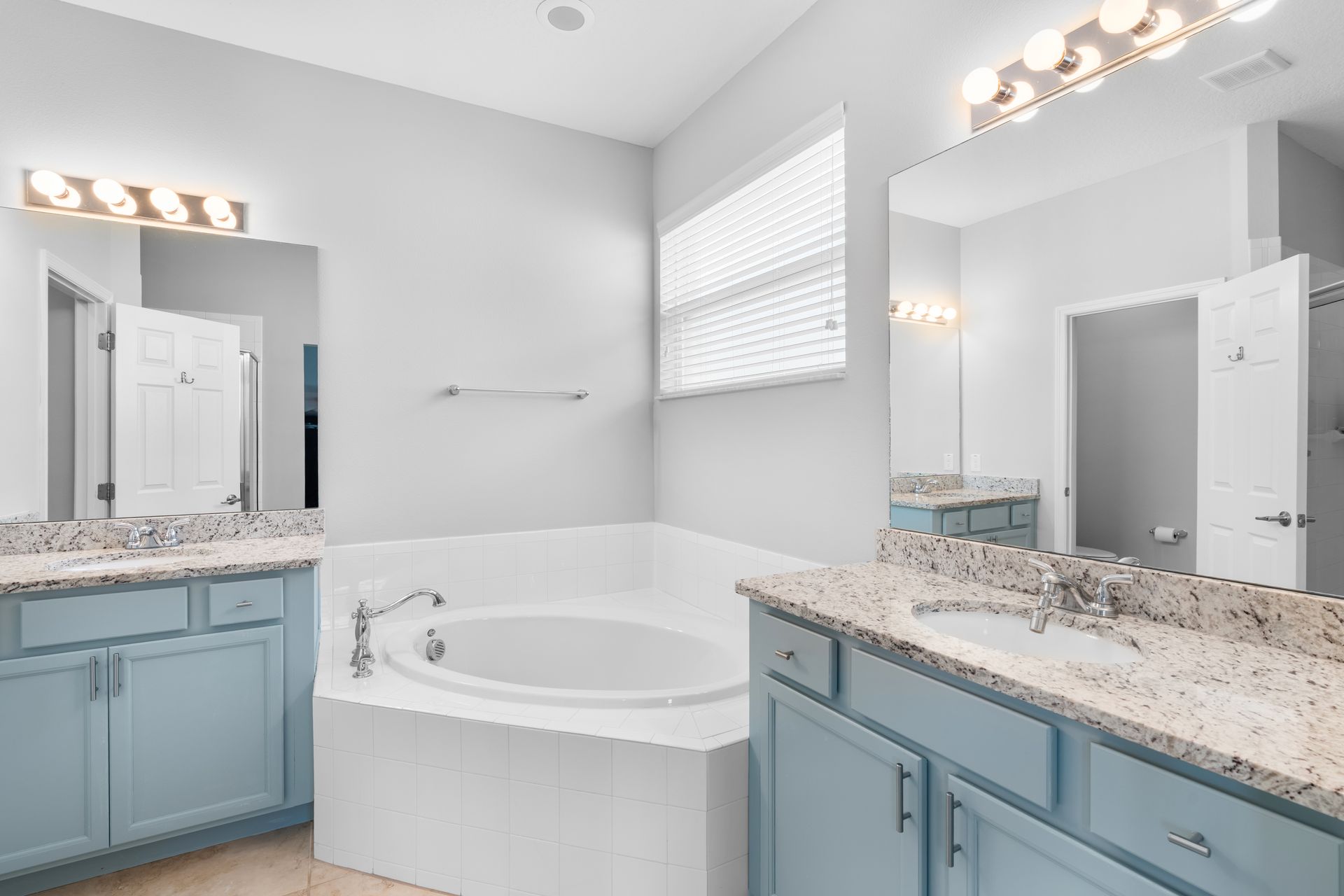 Bathroom with blue cabinets, white tub, mirrors, and lights.