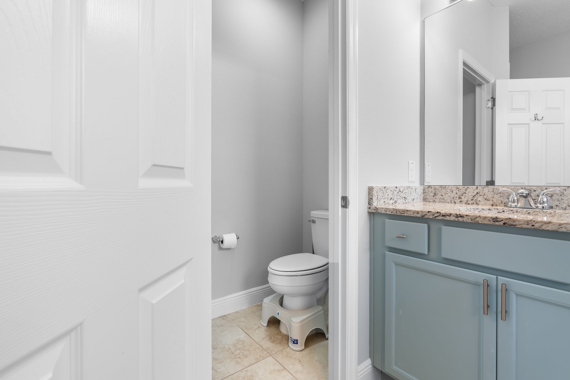 Bathroom with blue vanity, toilet, and step stool for accessibility.