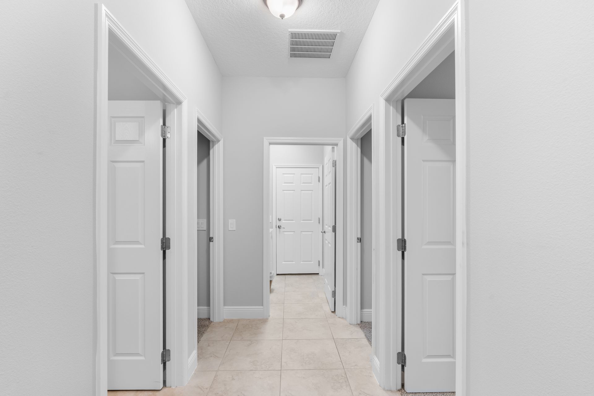 Hallway with several white doors, light-colored floor, and overhead lighting.