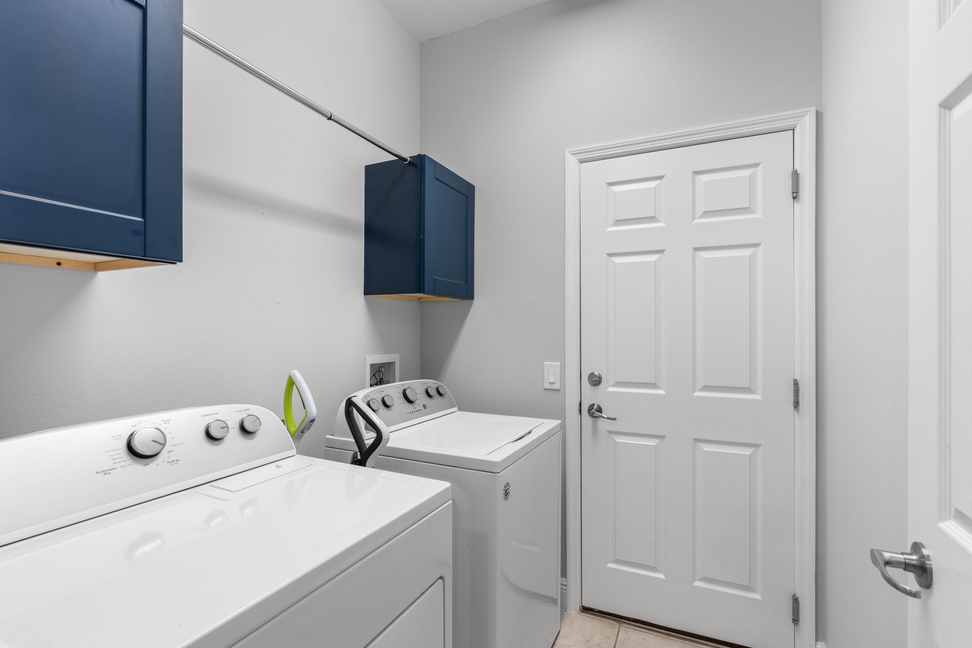 Laundry room with blue cabinets, white appliances, and a white door.
