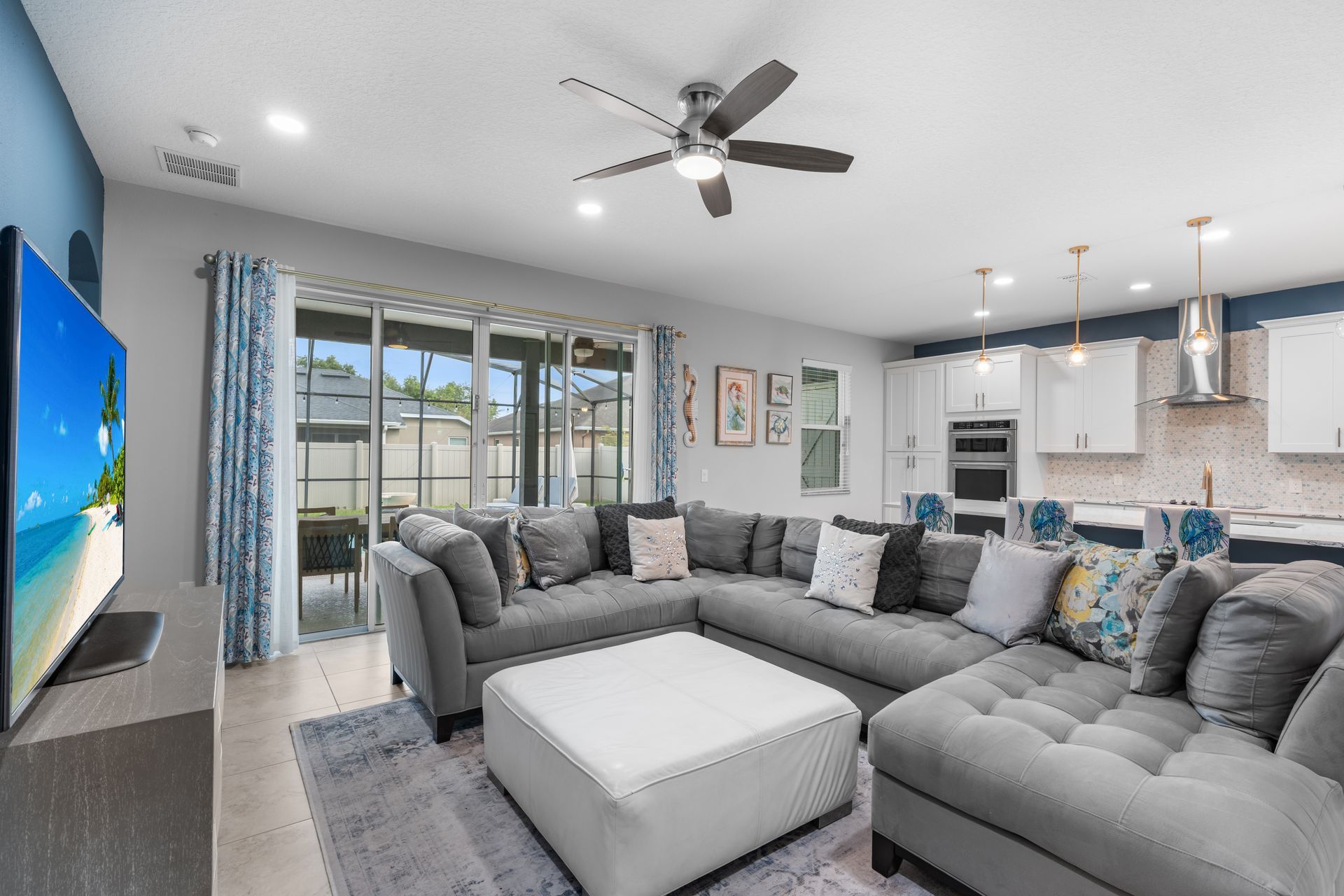 Living room with gray sectional sofa, large TV, and open kitchen with bright decor.