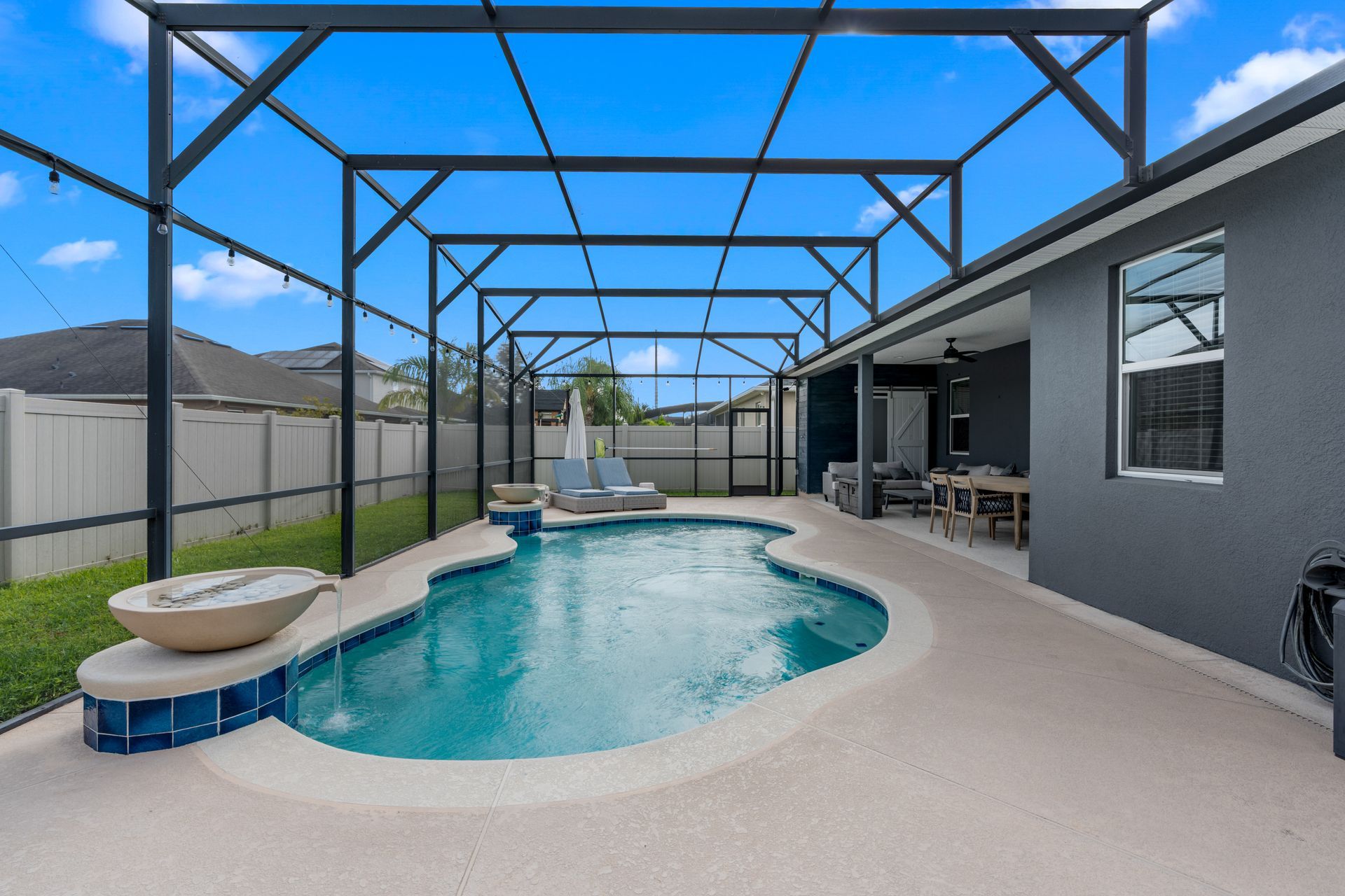 Pool area with turquoise water, concrete patio, and dark screen enclosure against blue sky.