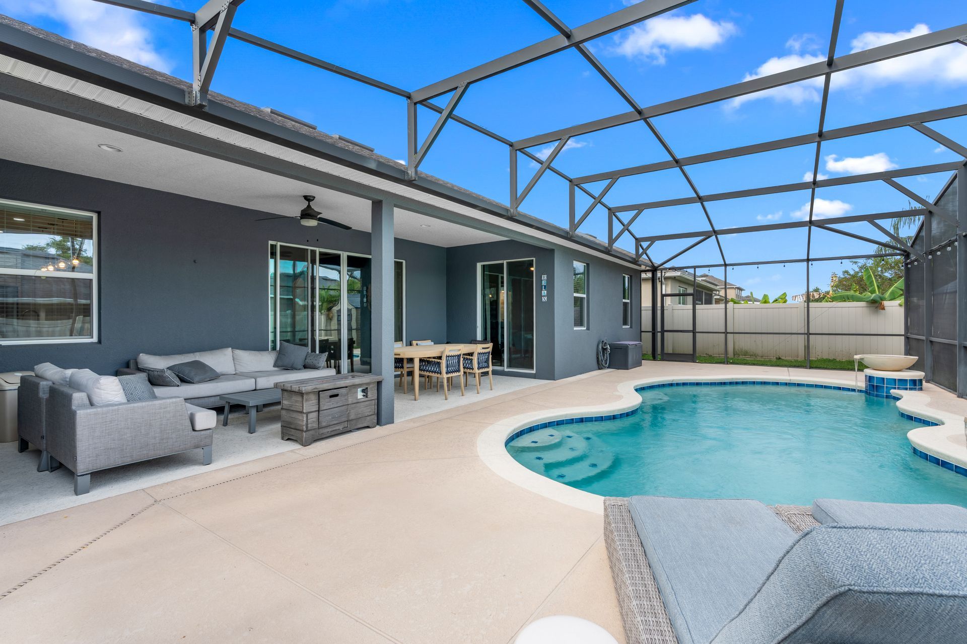 Backyard with pool, patio, gray furniture, and screened enclosure under a blue sky.