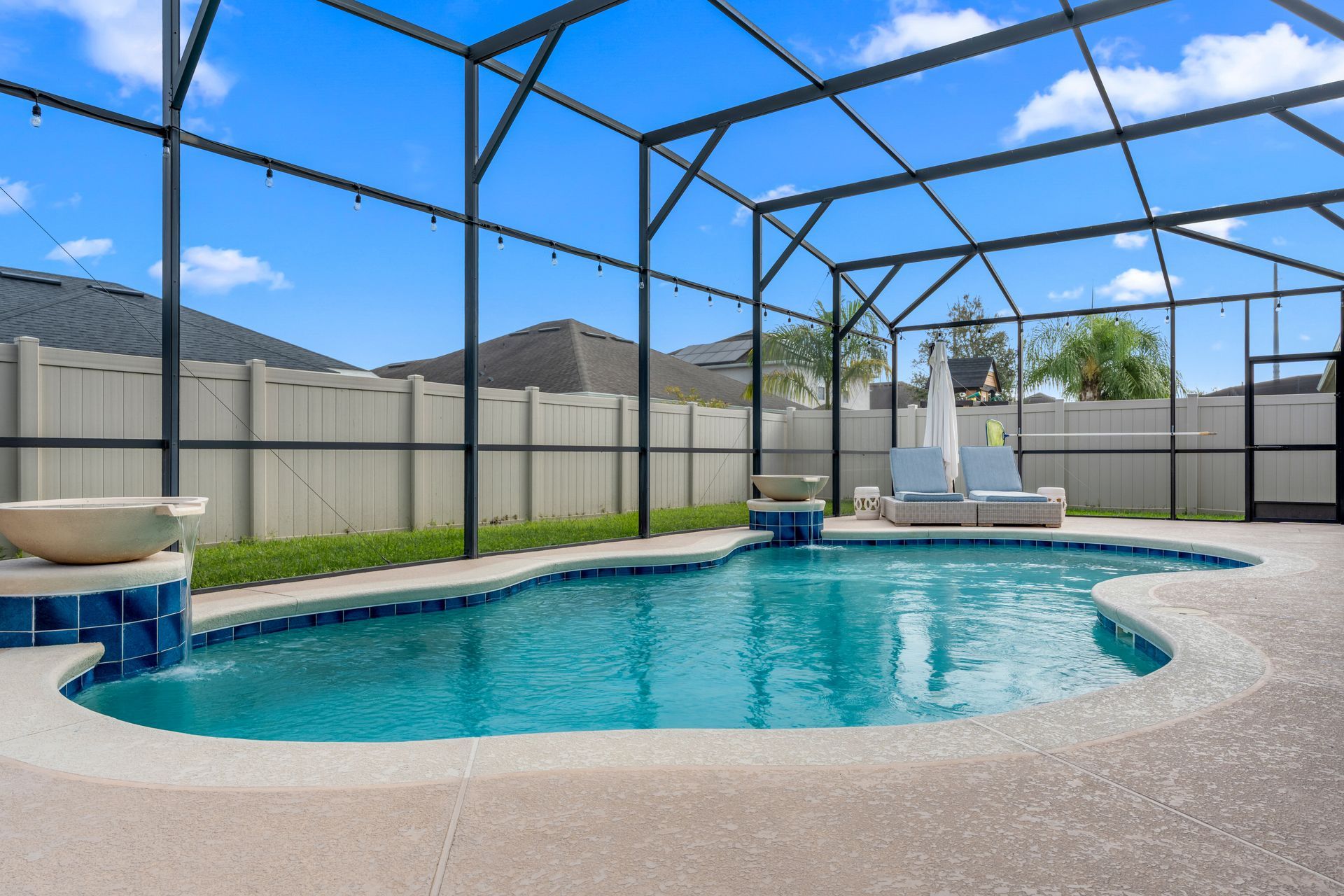 Swimming pool enclosed in a screened patio with lounge furniture under a blue sky.