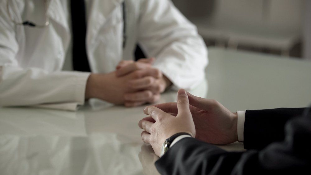 Doctor in white coat sits across from a person in a suit at a table, hands clasped — Endoscopist & General Surgeon in Mackay, QLD