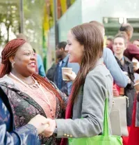 People networking at an outdoor event, shaking hands and talking while holding coffee cups.