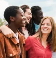 A group of friends laughing and smiling outdoors, close together in a candid, joyful moment.