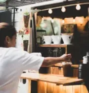 A person in a white shirt reaching for a cup at a mobile coffee cart with warm string lighting.
