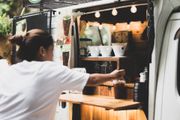 A person in a white shirt reaching for a cup at a mobile coffee cart with warm string lighting.