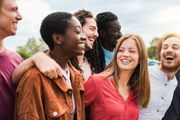 A group of friends laughing and smiling outdoors, close together in a candid, joyful moment.