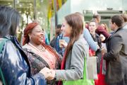 People networking at an outdoor event, shaking hands and talking while holding coffee cups.