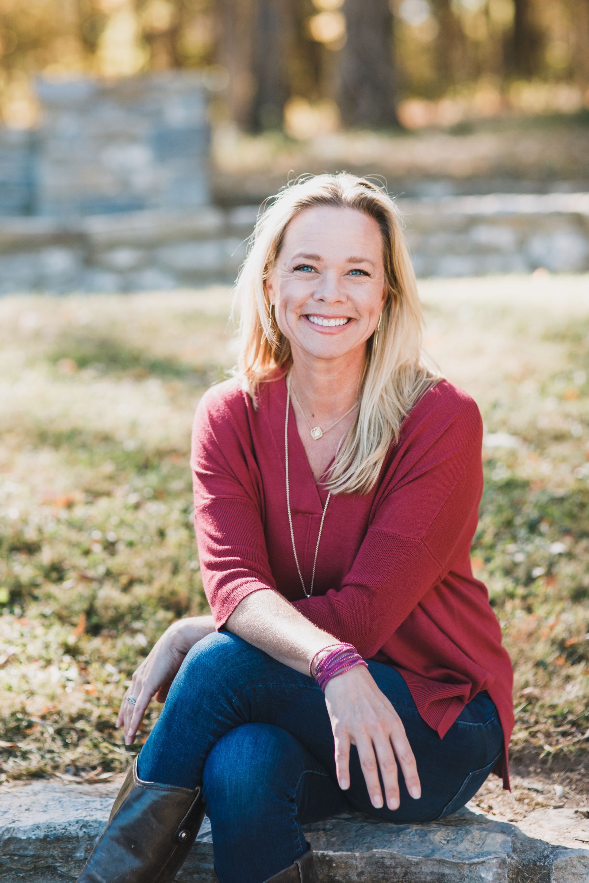 A woman is sitting on a rock in a park and smiling.