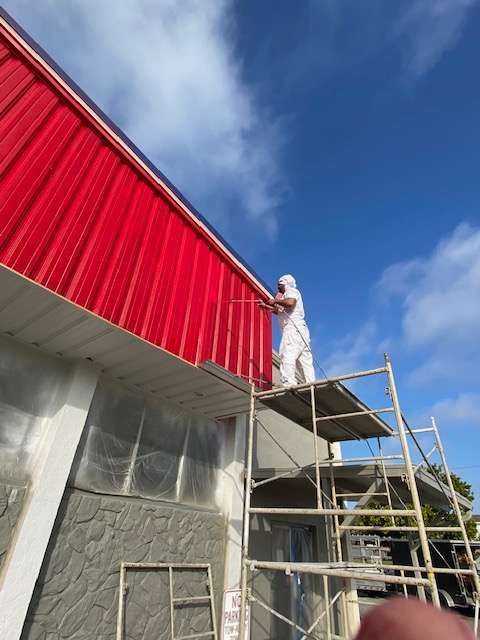 A man is painting a red roof of a building