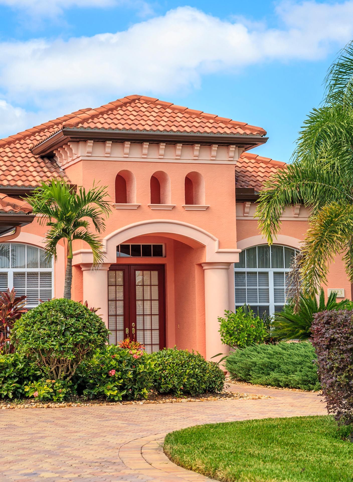 A large pink house with a tile roof and a brick driveway.