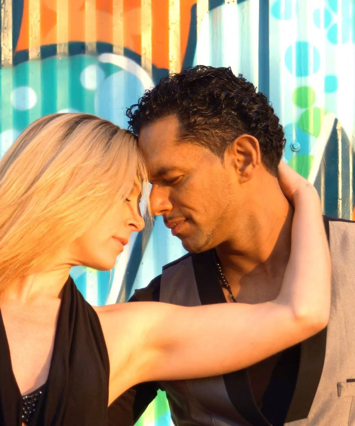 A man and a woman are hugging in front of a graffiti wall