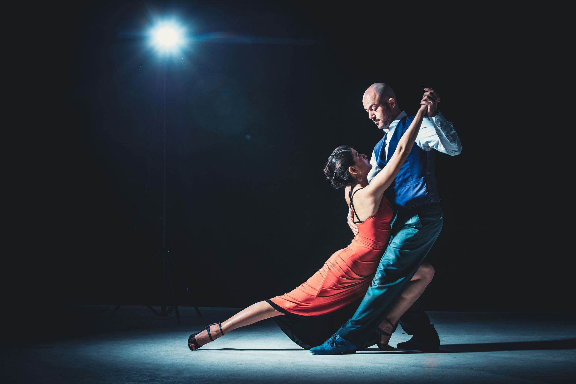 A man and a woman are dancing tango in a dark room.