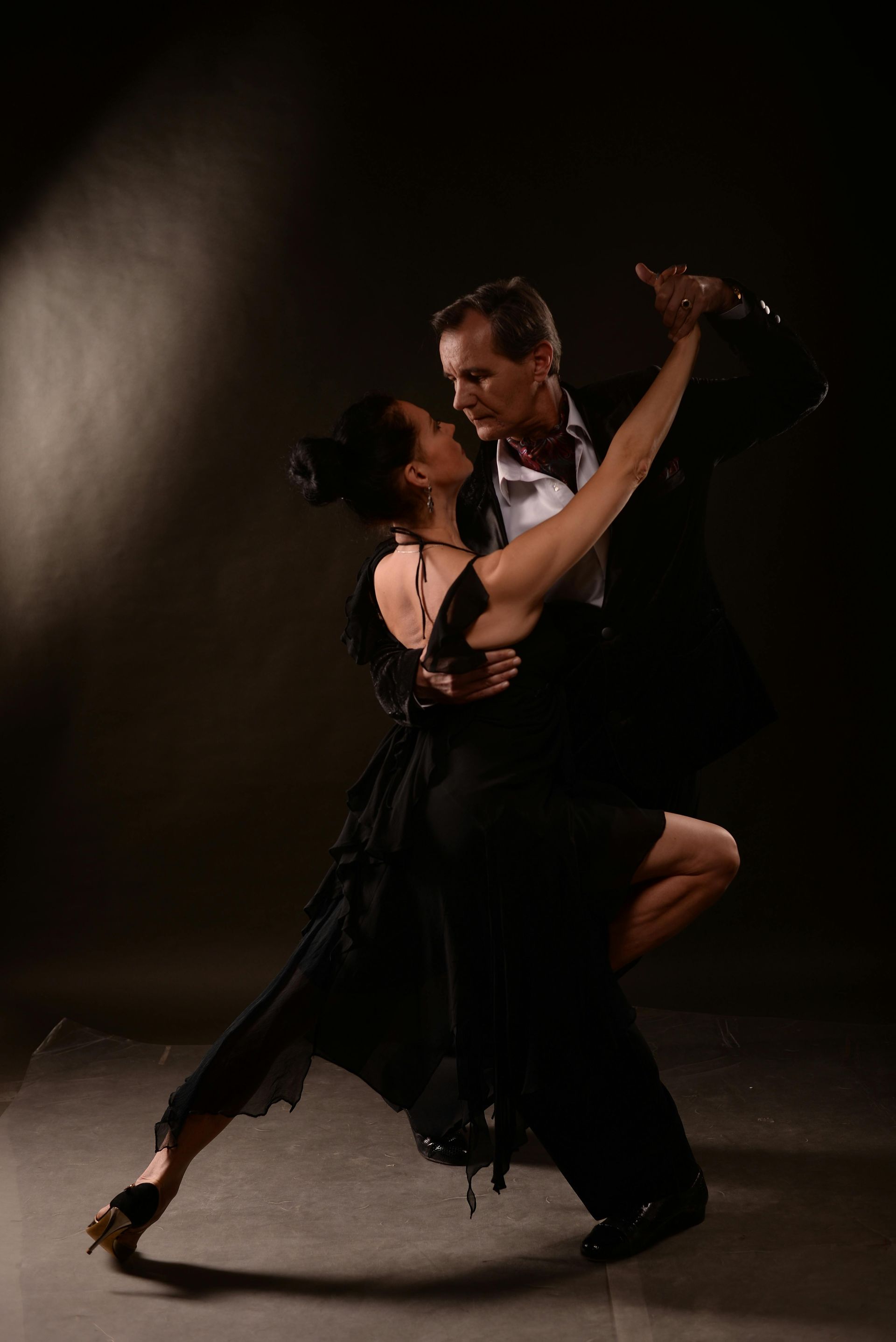A man and a woman are dancing tango in a dark room.