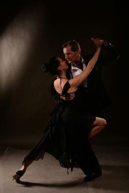 A man and a woman are dancing tango in a dark room.