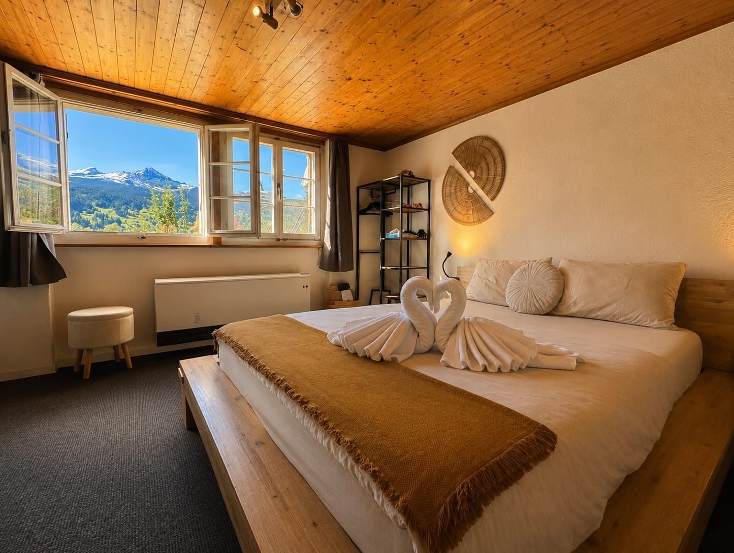 Gemütliches Schlafzimmer mit großem Bett, Holzdecke und Bergblick durch ein offenes Fenster