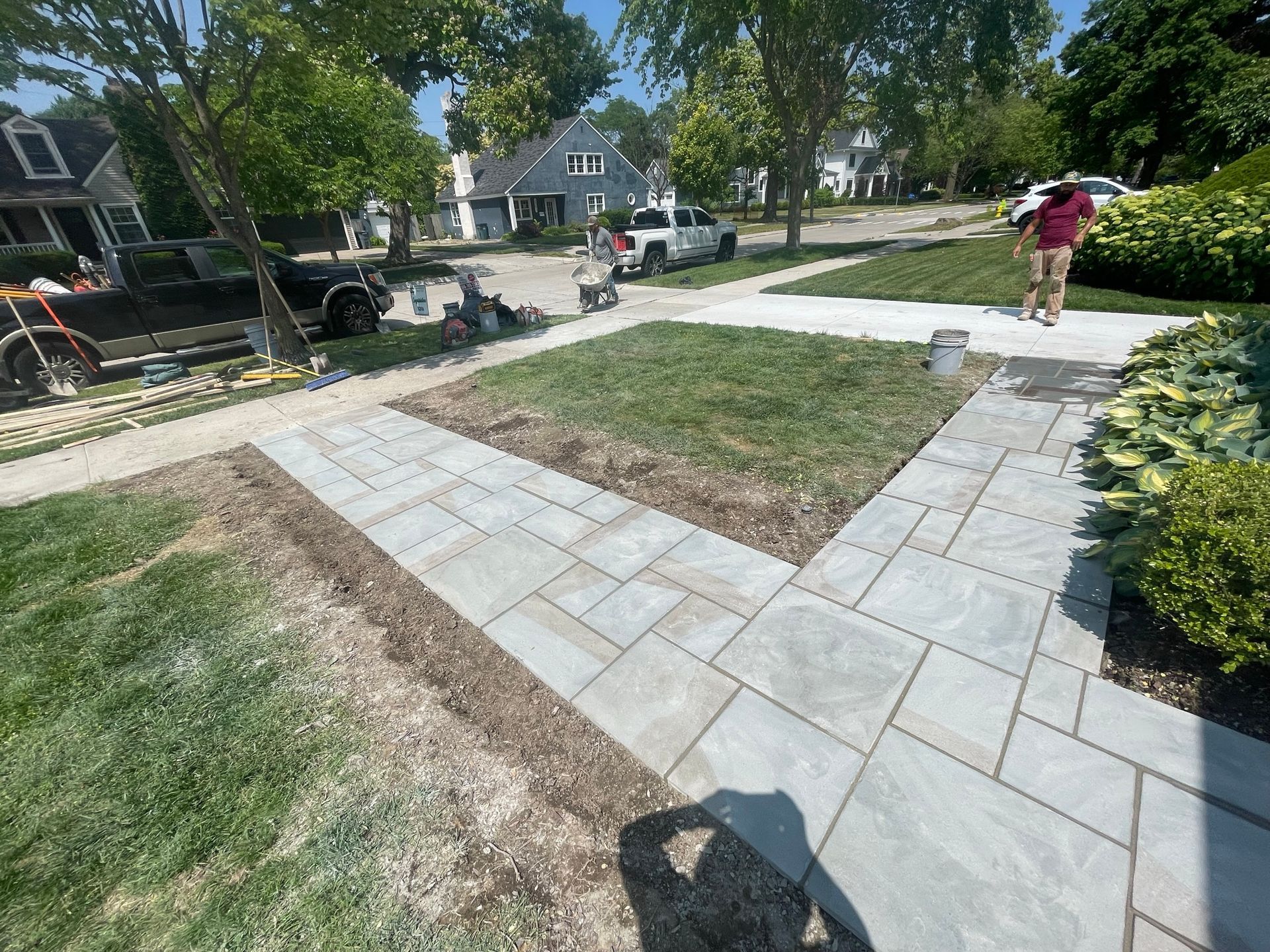 A newly-installed stone walkway in a front yard. A worker in a red shirt carries a bucket.