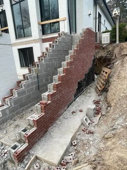 Construction site with brick and cinder block staircase against a white building. Brickwork is partially completed, revealing building materials.
