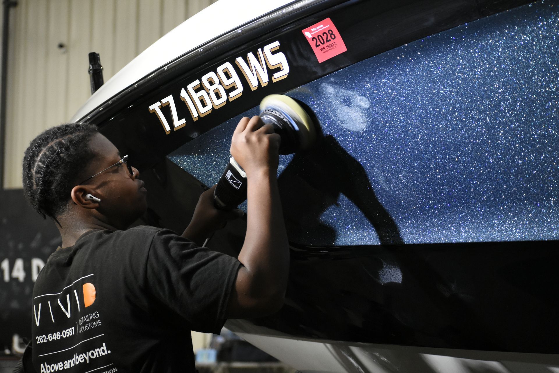 A person polishes the side of a black boat with a power tool in a workshop.