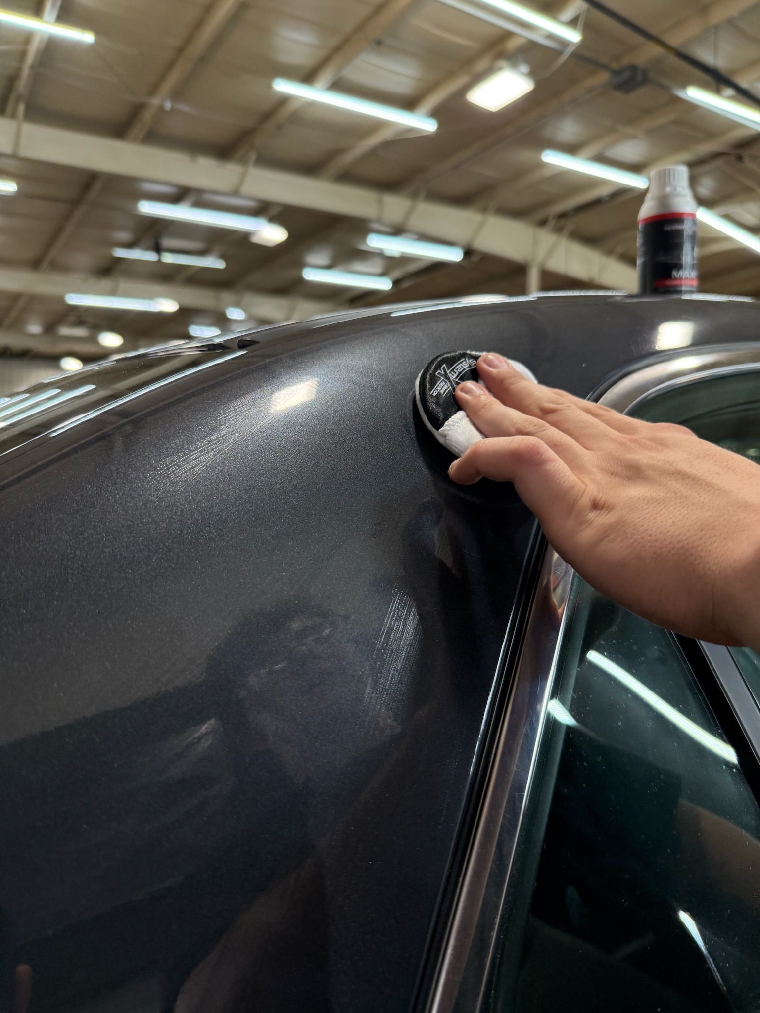 Hand applying detailing product to the roof of a dark gray car in a garage.
