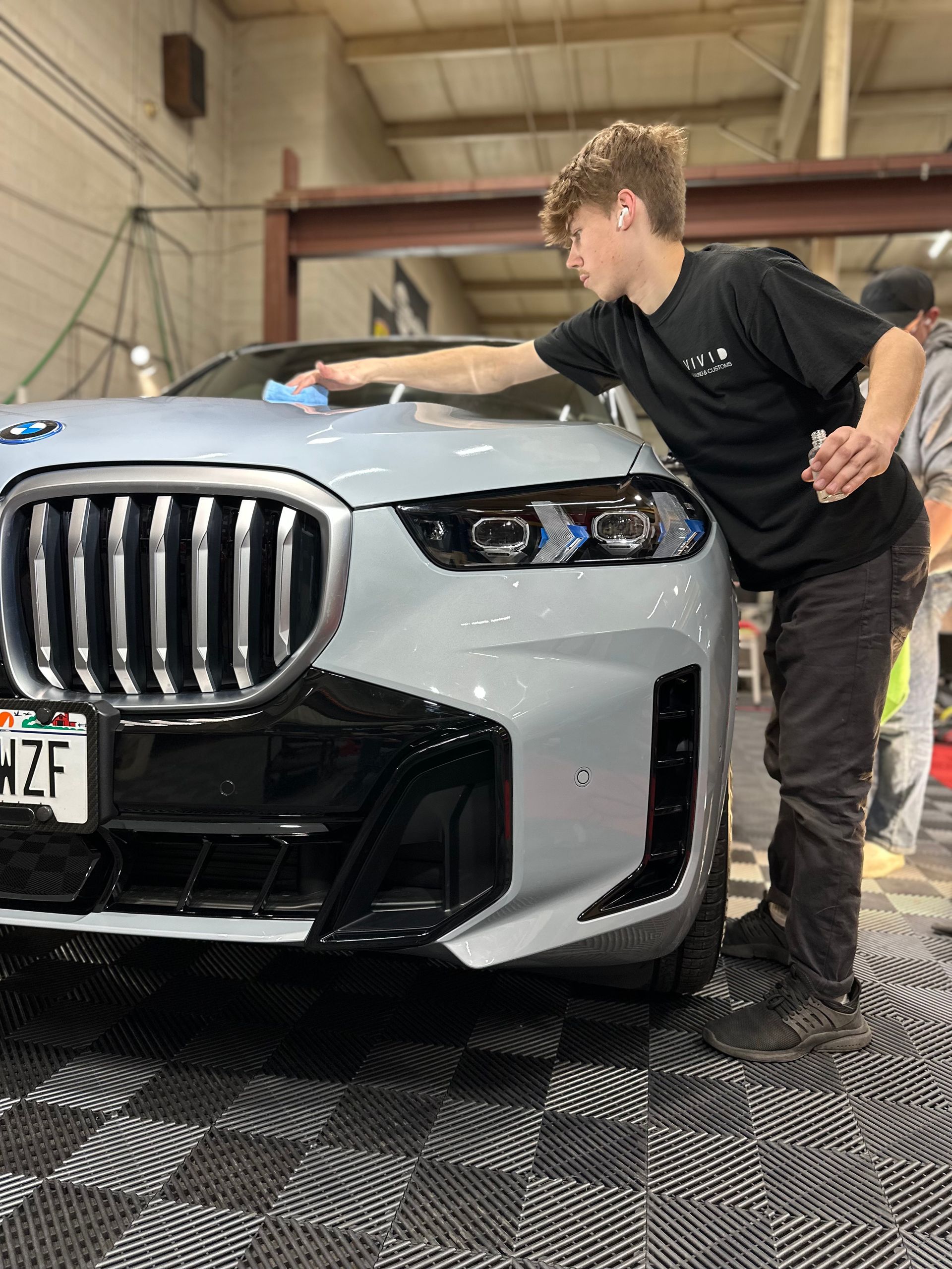 Young man waxing a light gray BMW inside a garage.
