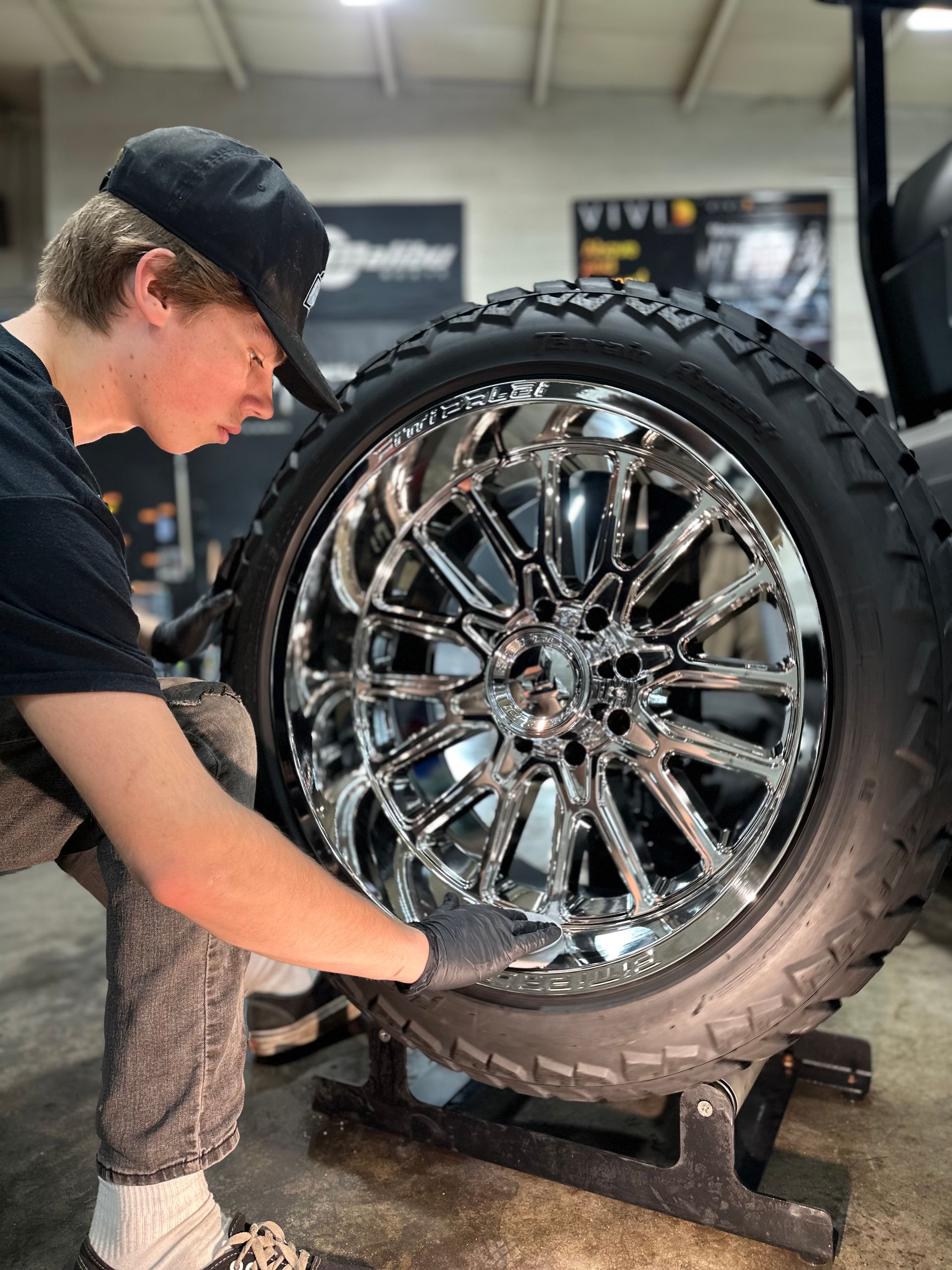 Young person inspecting a chrome rim and tire. They are in a garage-like setting, looking closely at the wheel.