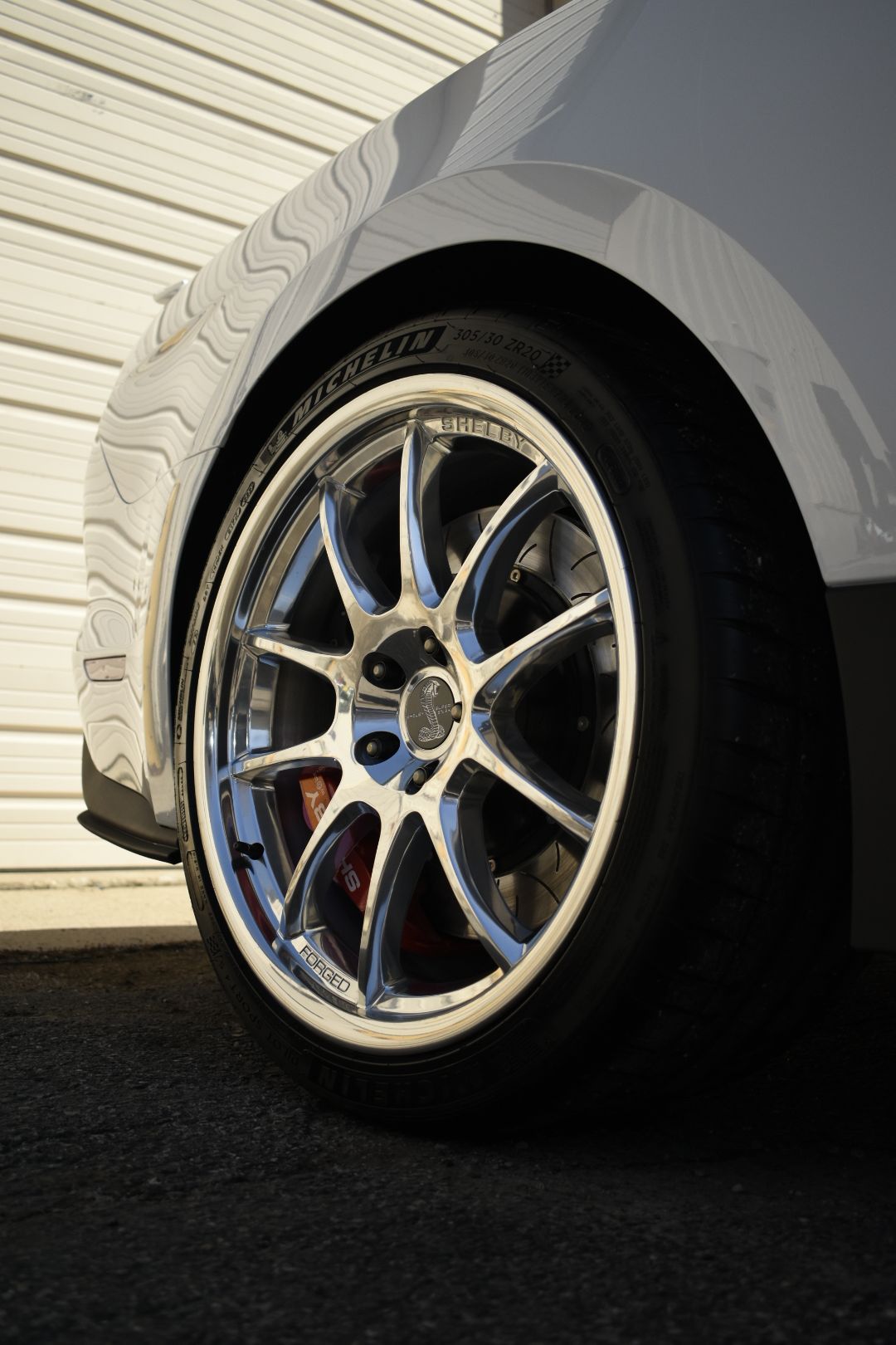 Silver car wheel with a chrome rim, black tire, and a red brake caliper.