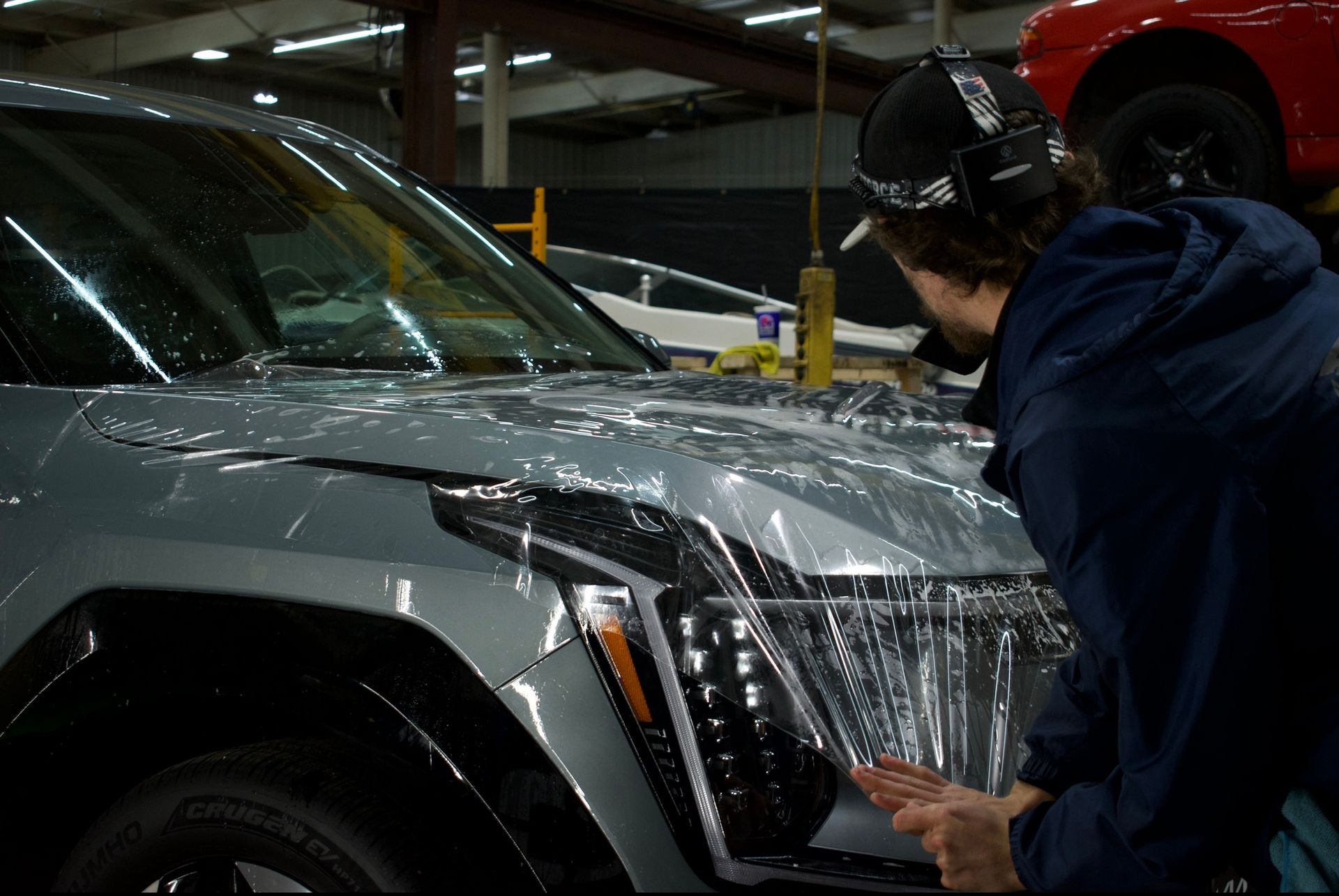 Person applying protective film to the hood of a light-blue SUV in a garage.