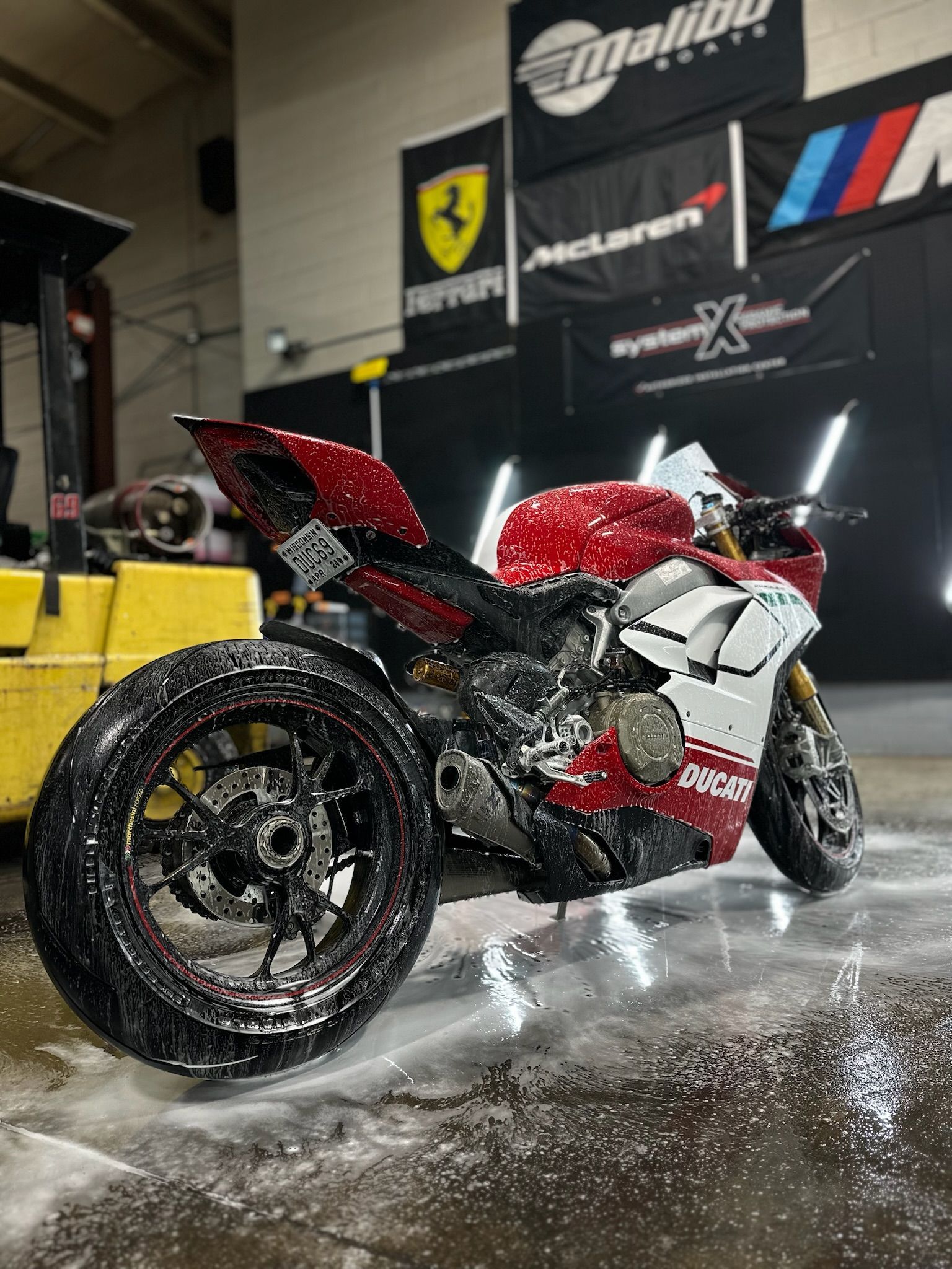 Red and white Ducati motorcycle being washed, in a shop with racing flags and logos in the background.