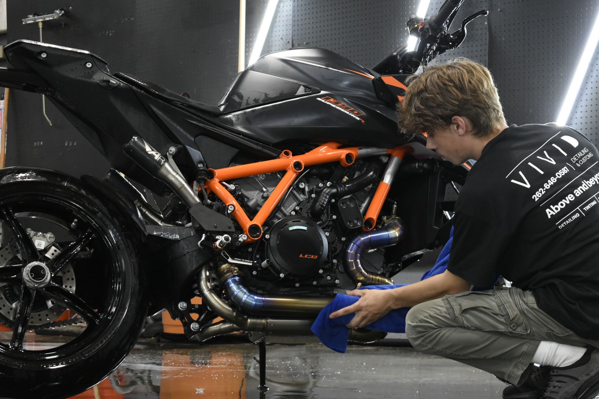 Person cleaning a black and orange motorcycle with a blue cloth.