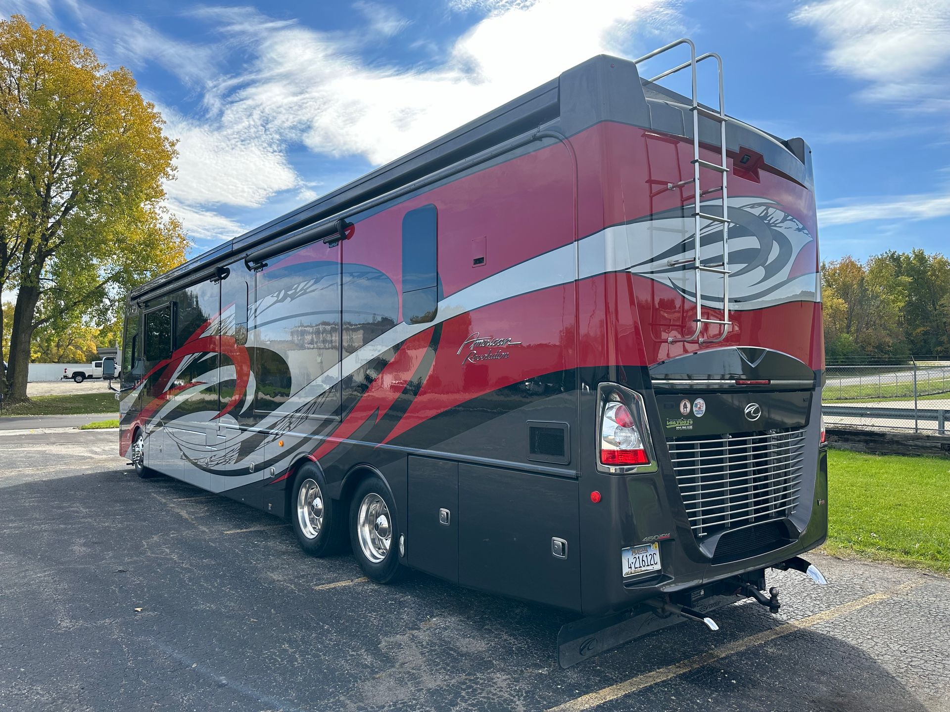 Luxury RV with red, silver, and black paint parked on asphalt under a partly cloudy sky.