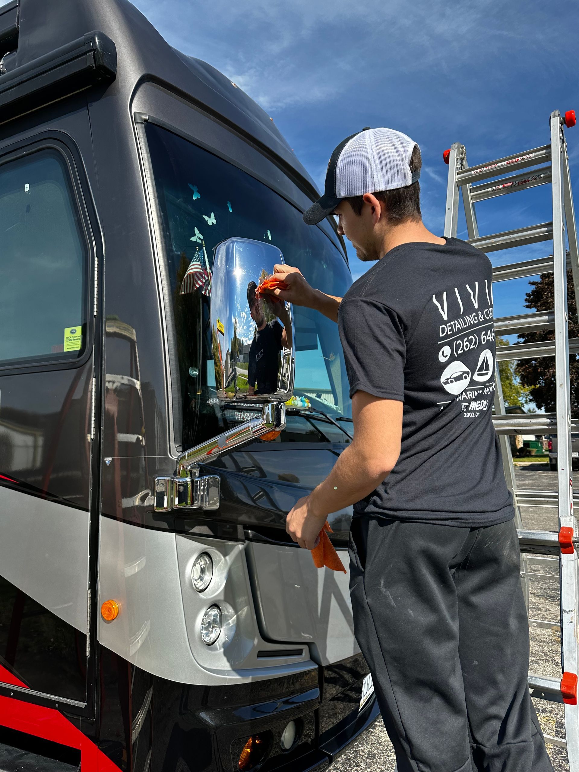 Man cleaning the windshield of a large RV on a sunny day.