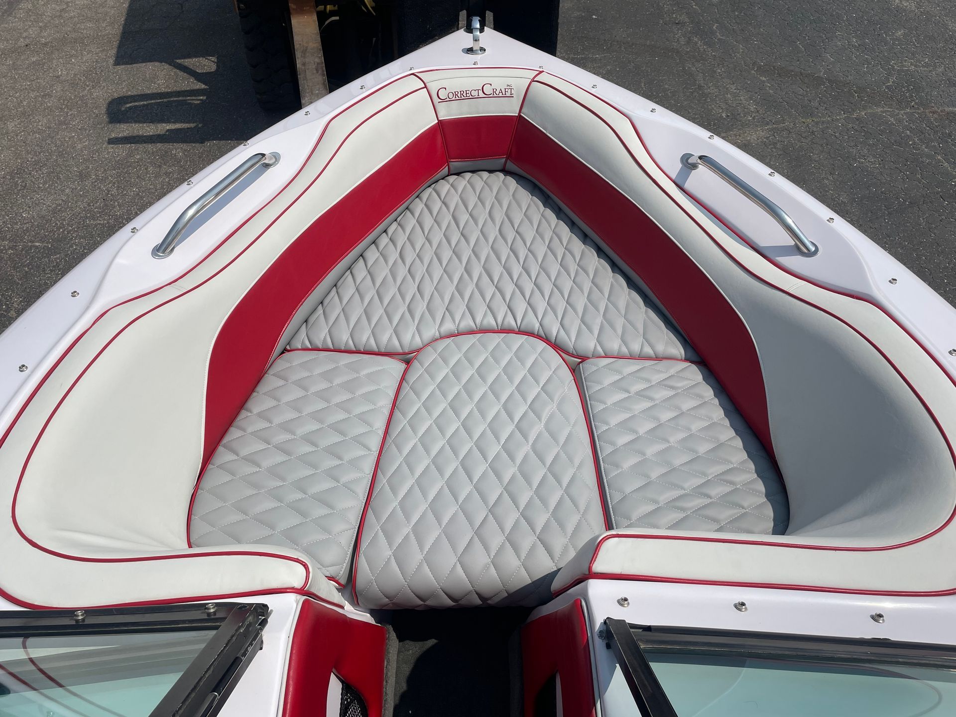 Boat's bow with white, diamond-stitched gray seats and red trim. Stainless steel handrails and windshields visible.