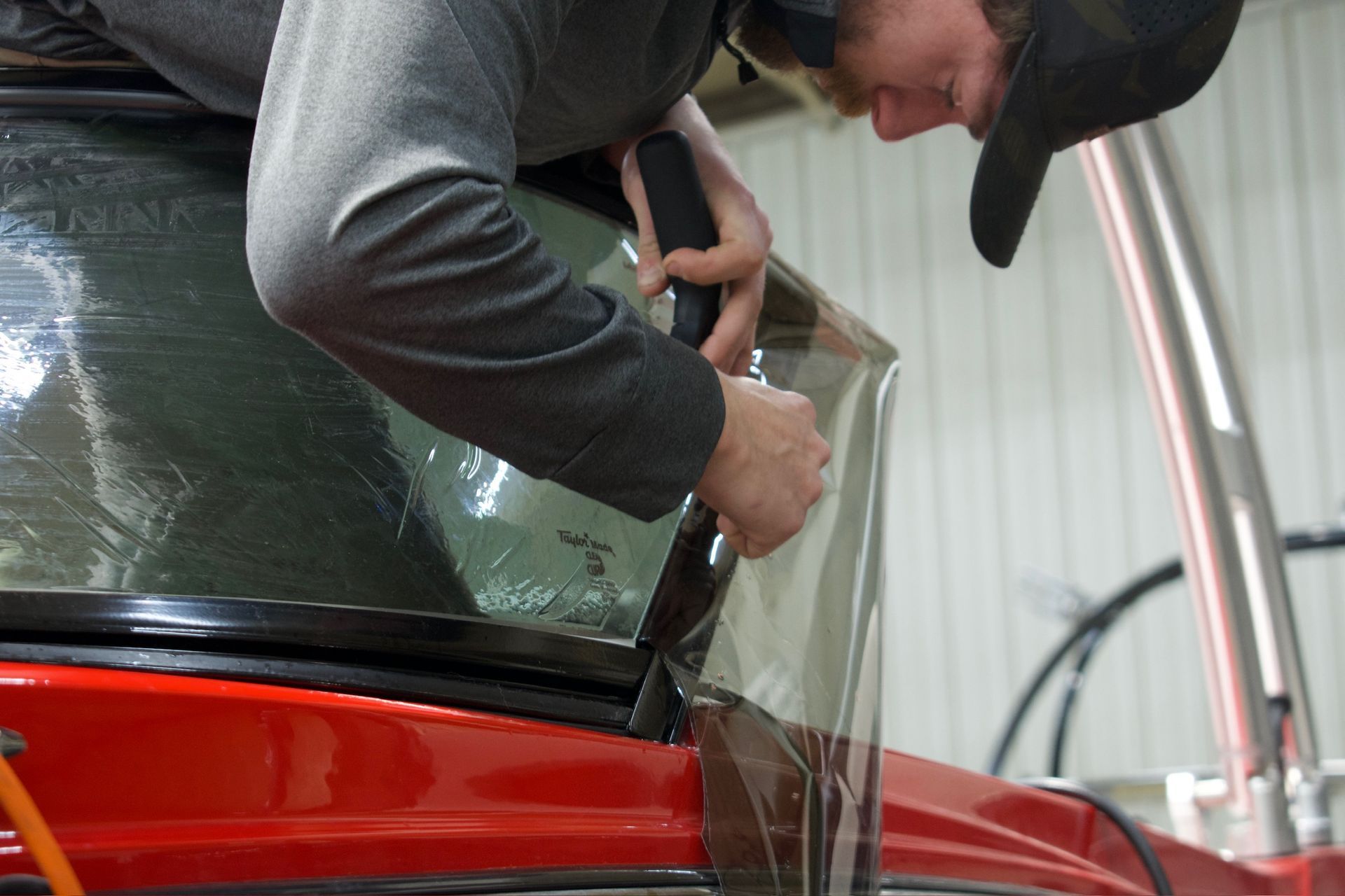Person wearing a hat applies tinted film to a car window, indoors.