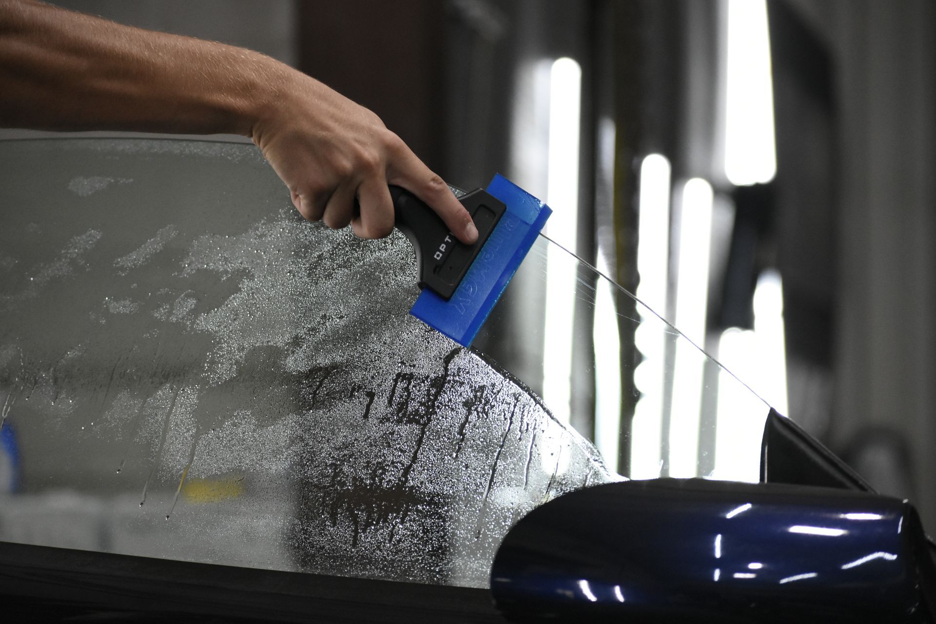 A person applying tint film to a car window using a blue squeegee in a workshop.