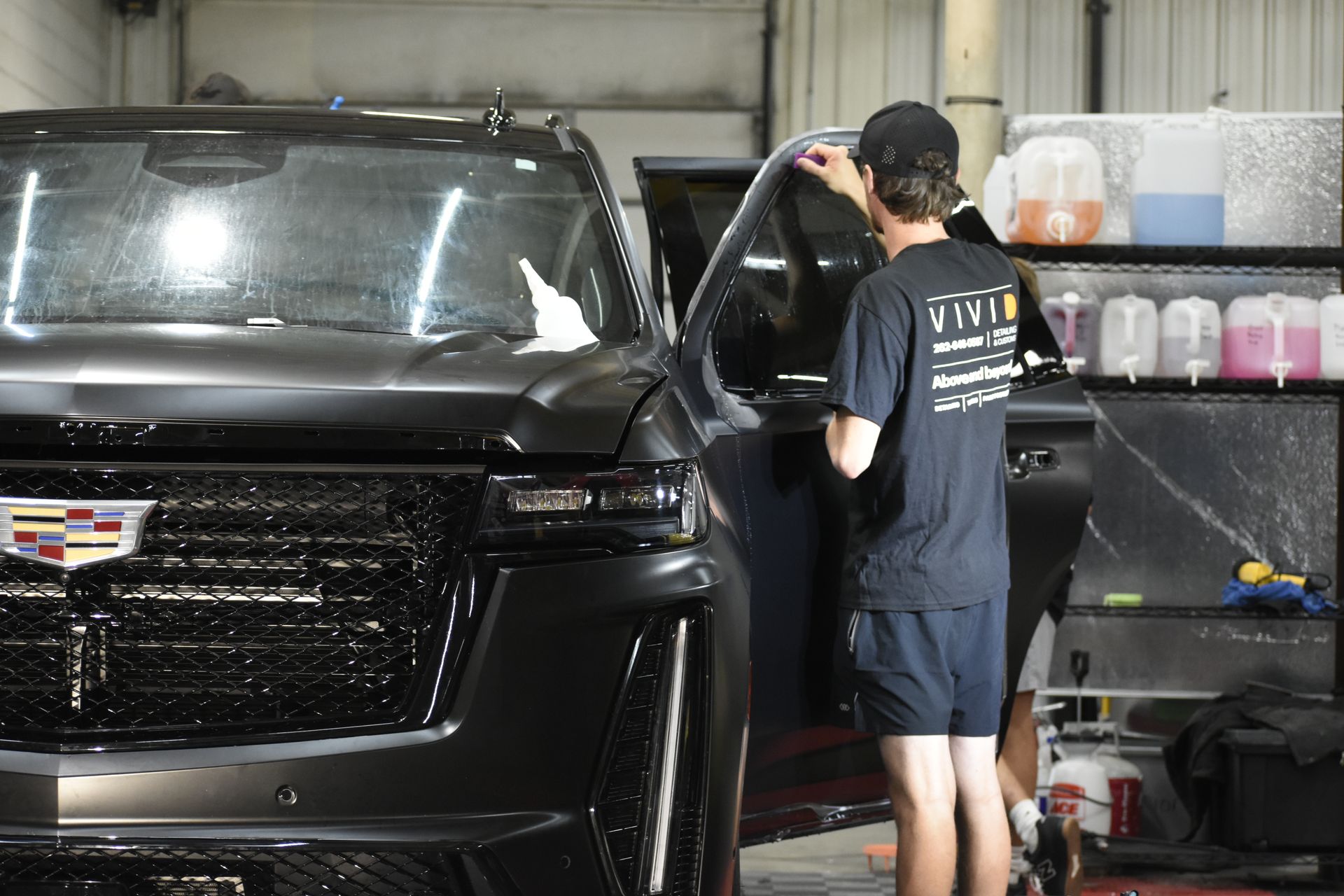 Man applying tint film to a black SUV window inside a garage.