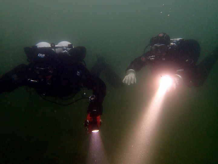 Deux plongeurs nagent dans l'eau et l'un d'eux tient une lampe de poche