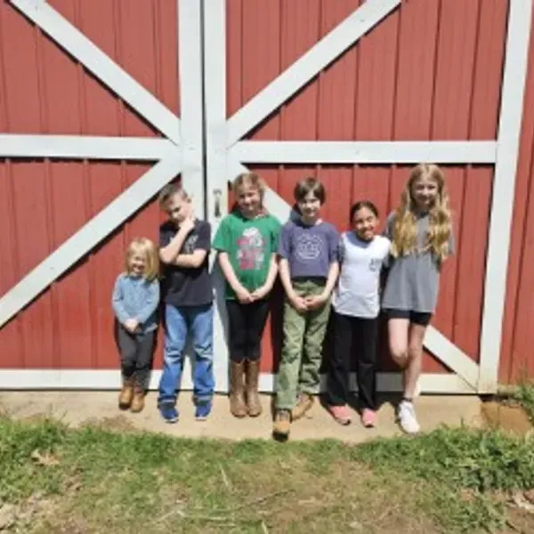 A woman in an apron and yellow gloves is holding a plate and a sponge.