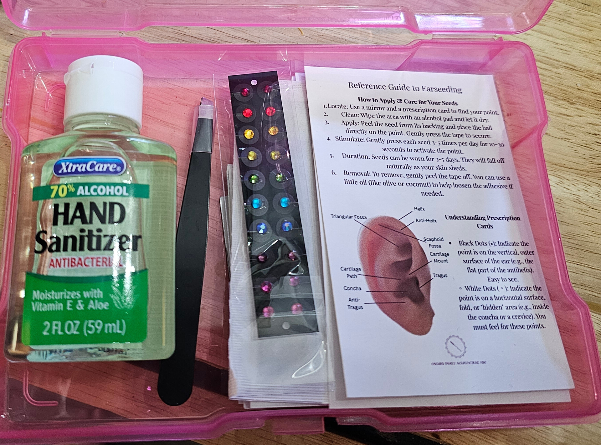 Pink plastic container with hand sanitizer, tweezers, ear charts, and earseed strips