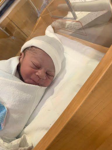 Newborn baby wrapped in a white blanket and hat, sleeping in a wooden bassinet.