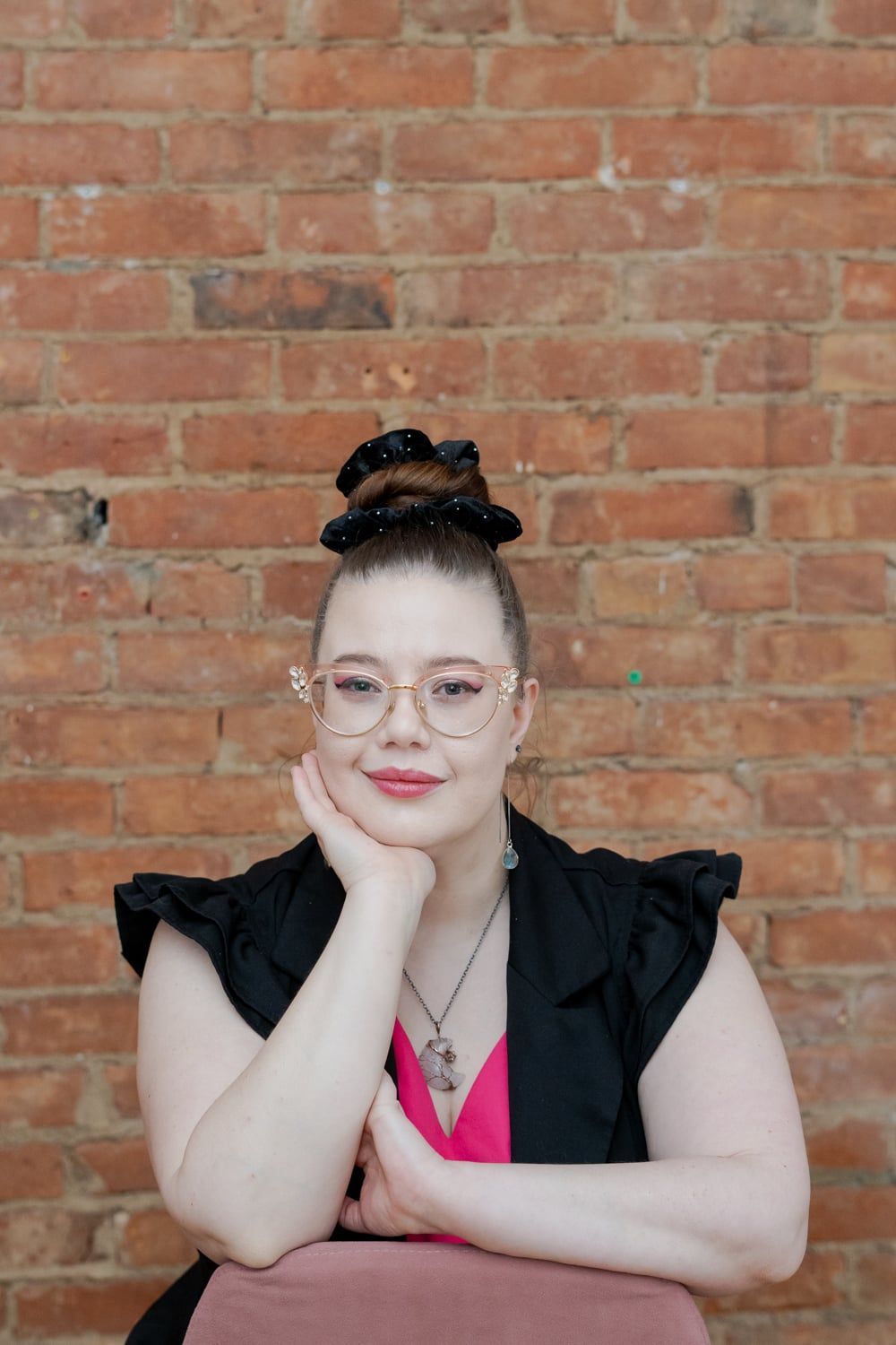 Woman in pink sweater, holding baby in red polka-dot overalls under blossoming tree.