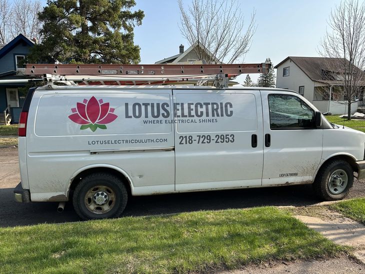 White Lotus Electric van with ladder, logo and phone number, parked on a street.