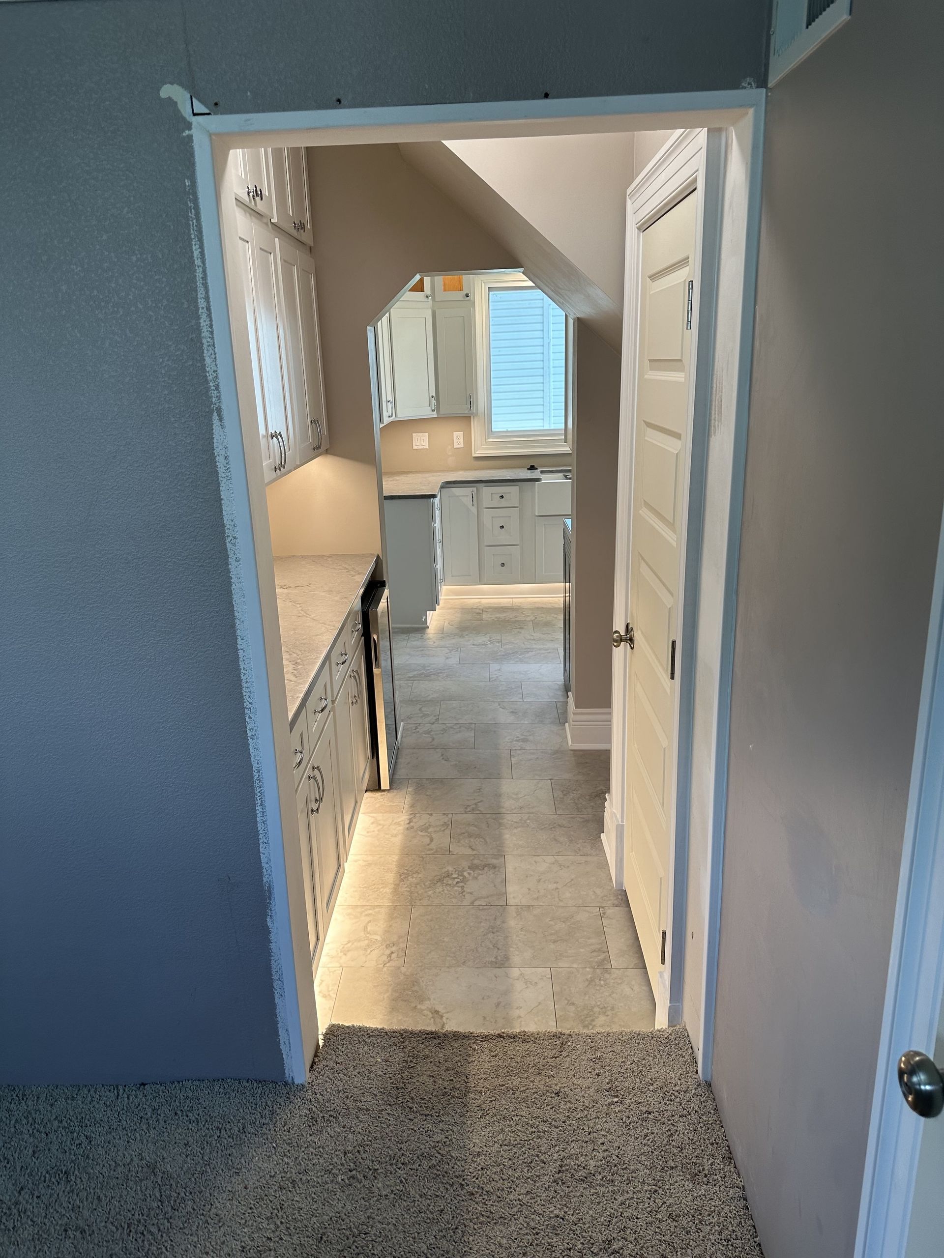 View into a kitchen from a doorway. Beige walls and gray flooring. Kitchen features countertops and cabinets.