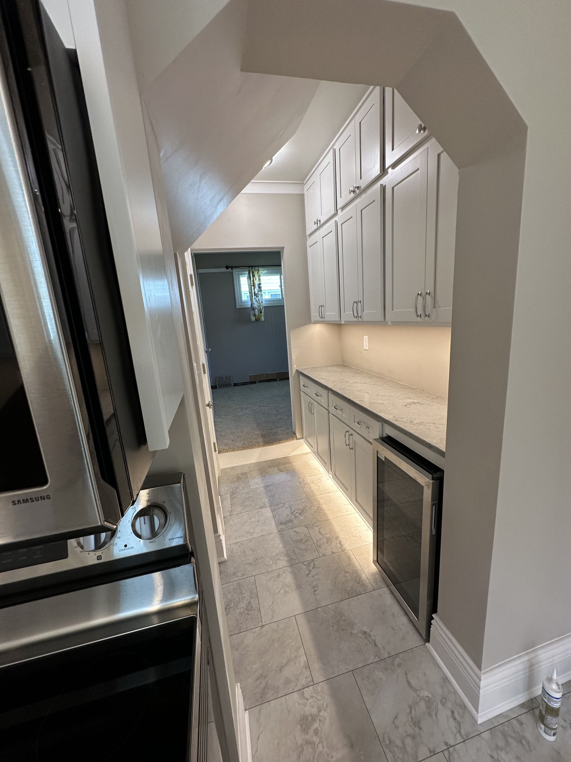 Gray cabinets with white countertops, under-cabinet lighting, and a wine cooler in a kitchen.